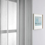 Rideau gris clair pour un salon moderne, suspendu près d'une fenêtre, ajoutant une touche d'élégance et de luminosité à l'intérieur. Accessoire de décoration idéal pour les espaces contemporains, complétant parfaitement un tableau encadré au mur. Optimisation de la lumière naturelle pour un style épuré et chic.