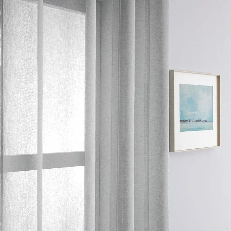 Rideau gris clair pour un salon moderne, suspendu près d'une fenêtre, ajoutant une touche d'élégance et de luminosité à l'intérieur. Accessoire de décoration idéal pour les espaces contemporains, complétant parfaitement un tableau encadré au mur. Optimisation de la lumière naturelle pour un style épuré et chic.