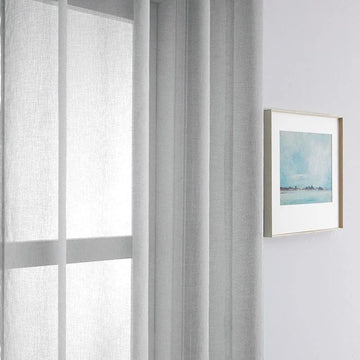 Rideau gris clair pour un salon moderne, suspendu près d'une fenêtre, ajoutant une touche d'élégance et de luminosité à l'intérieur. Accessoire de décoration idéal pour les espaces contemporains, complétant parfaitement un tableau encadré au mur. Optimisation de la lumière naturelle pour un style épuré et chic.