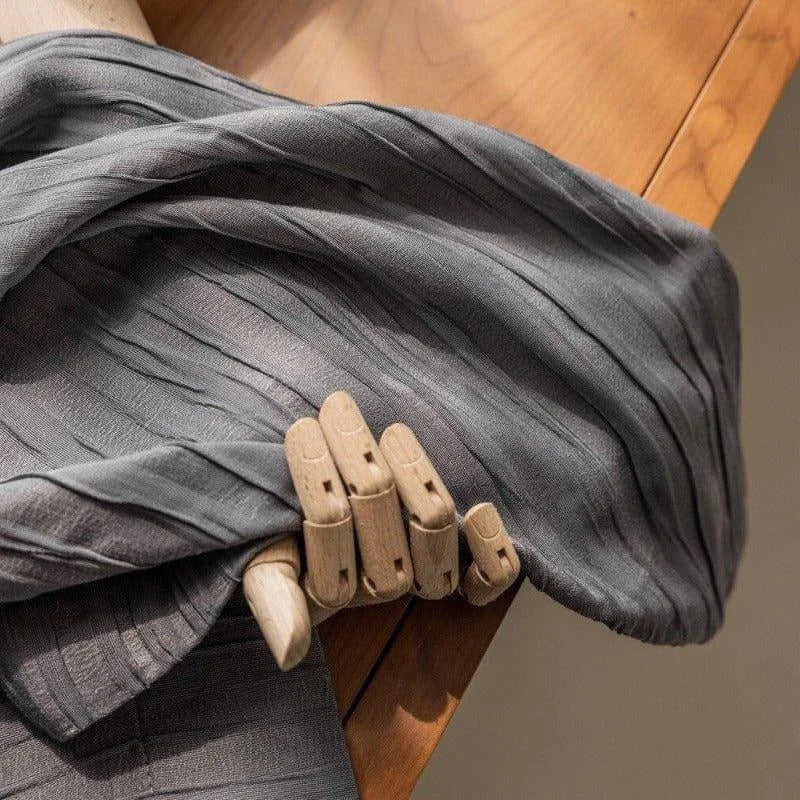 Étoffe élégante grise drapée sur un banc en bois, tenue délicatement par une main articulée en bois, idéale pour les projets de couture créatifs et la décoration intérieure moderne.