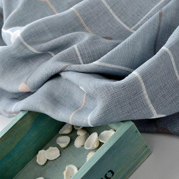 Étoffe à motif à carreaux gris-bleu drapée à côté d'une boîte en bois turquoise contenant des petits coquillages blancs.