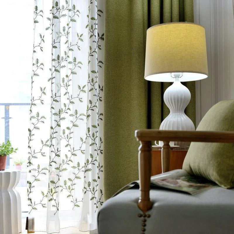 Luminaires élégants et rideaux design pour salon moderne. Lampe de table blanche au style contemporain, posée sur une table en bois. Rideaux vert olive et voilage à motifs floraux apportant une ambiance chaleureuse et naturelle à la pièce. Idéal pour la décoration intérieure et l'éclairage du séjour.