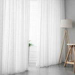 Rideaux blancs transparents suspendus dans un salon moderne, illuminant la pièce avec une lumière douce et naturelle. Ambiance épurée et élégante rehaussée par une lampe sur trépied et un décor minimaliste. Parfaits pour créer une atmosphère accueillante et lumineuse dans tout intérieur.