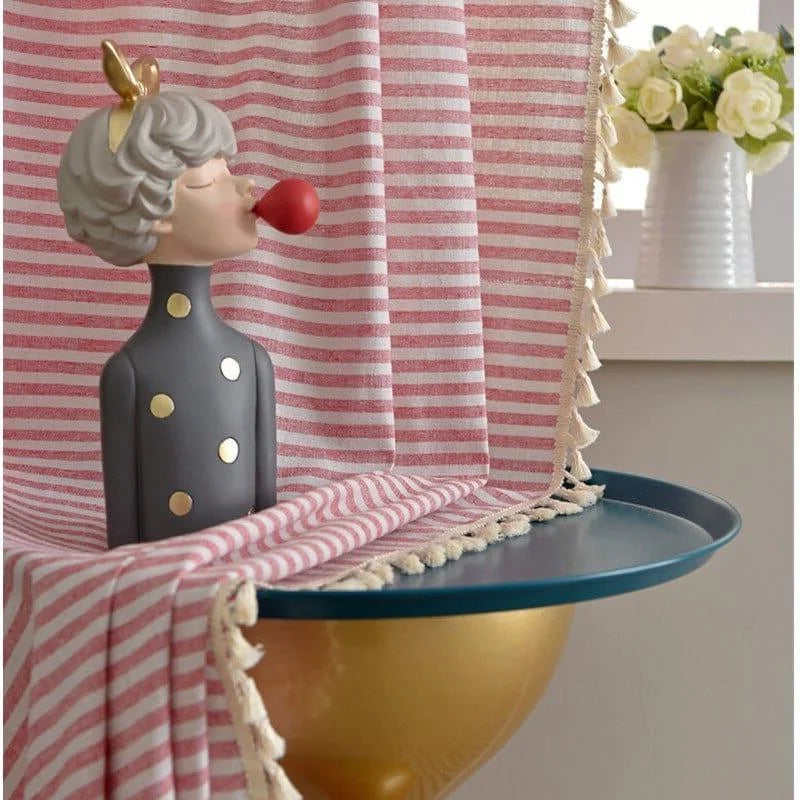 Statue décorative moderne avec motifs dorés, posée sur une surface bleue. Élément de design intérieur original, idéal pour ajouter une touche artistique à tout espace. Rideau à rayures roses et blanches en arrière-plan pour une ambiance chaleureuse. Bouquet de fleurs blanches dans un vase à proximité pour compléter le décor.