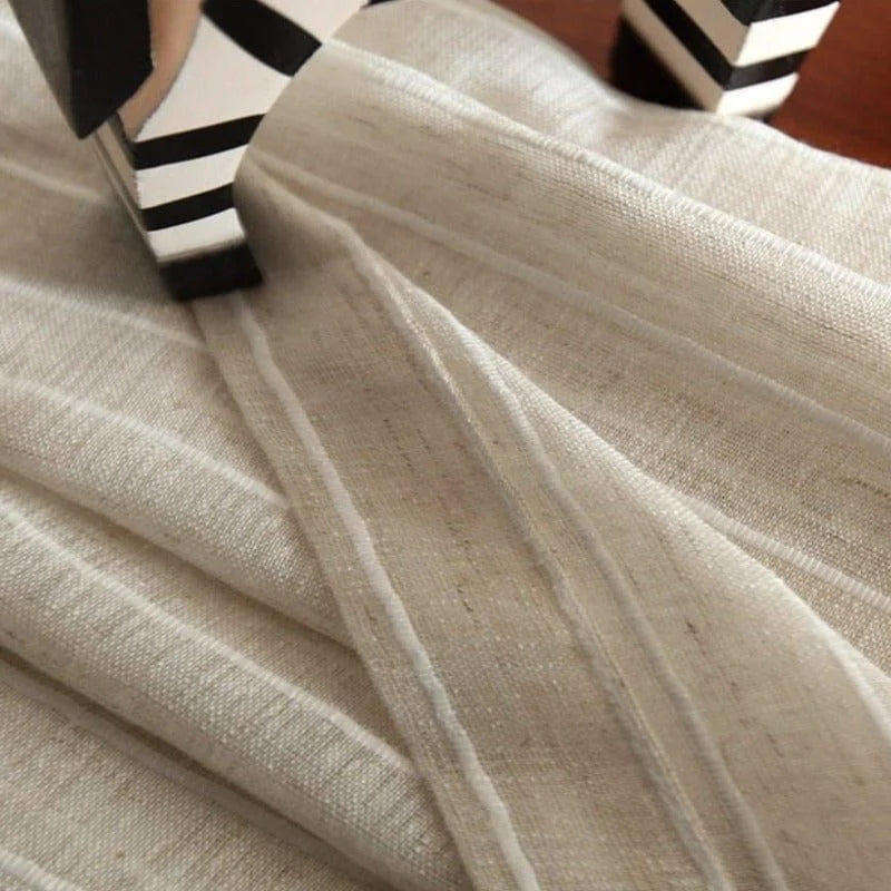 Image d'un tissu élégant à rayures, de couleur beige neutre, délicatement drapé sur une surface en bois. Idéal pour la décoration intérieure, ajoutant une touche sophistiquée et naturelle à tout espace. Parfait pour les rideaux, nappes ou autres projets décoratifs.