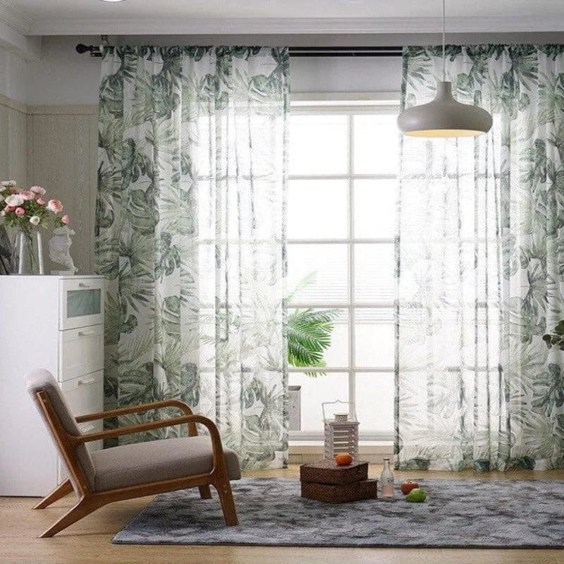 Rideaux tendance aux motifs végétaux verts dans un salon moderne. La décoration comprend un fauteuil contemporain en bois et tissu, une lampe suspendue design, et une commode blanche. Les rideaux laissent pénétrer la lumière naturelle, créant une ambiance lumineuse et apaisante, idéale pour un intérieur élégant et accueillant.
