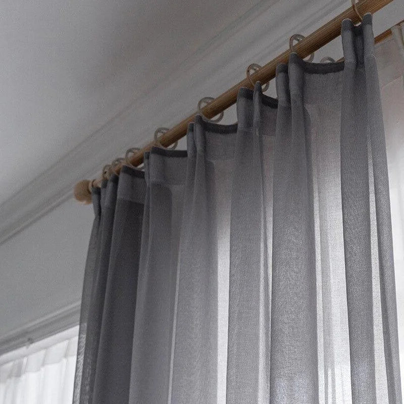 Rideau gris élégant suspendu à une tringle en bois, idéal pour ajouter une touche moderne à votre intérieur tout en préservant la luminosité de la pièce.