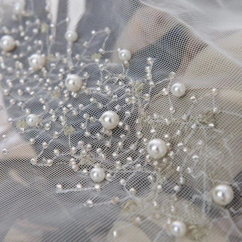Voile de mariée délicatement orné de perles blanches, idéal pour une cérémonie élégante. Accessoire de mariage avec détails raffinés pour sublimer votre tenue nuptiale. Design romantique et sophistiqué, parfait pour une allure chic et inoubliable lors de votre grand jour.