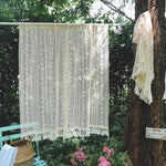 Rideau décoratif crochet beige suspendu dans un jardin verdoyant, idéal pour apporter une touche bohème à votre intérieur. Style artisanal avec franges, parfait pour créer une ambiance cosy et élégante. Parfait pour les salons, chambres ou espaces extérieurs couverts. Accessoire tendance pour personnaliser vos espaces avec charme et authenticité.