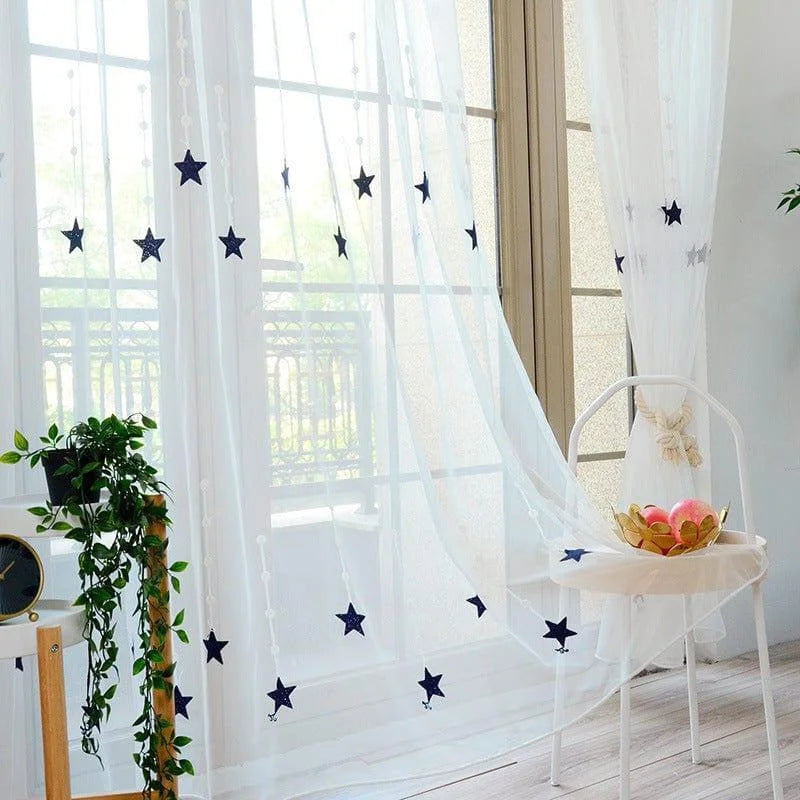 Rideau transparent avec motifs étoiles bleues, décorant une fenêtre lumineuse. Ce rideau ajoute une touche élégante et rêveuse à l'intérieur, filtrant la lumière du jour tout en permettant une ambiance apaisante. Idéal pour les chambres d'enfants ou pour un salon moderne, ce rideau décoratif transforme votre espace en un lieu accueillant et esthétique. Accessoire parfait pour personnaliser votre décoration intérieure avec raffinement.