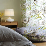 Rideau floral élégant dans une chambre moderne, ajoutant une touche de nature et de fraîcheur à l'espace. Le motif floral vibrant illumine la pièce, complété par une lampe de chevet design sur une table en bois, créant une ambiance chaleureuse et accueillante. Idéal pour une décoration intérieure harmonieuse et apaisante.