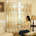 Femme assise dans un salon beige, observant un voilage vintage beige à motifs floraux classiques.