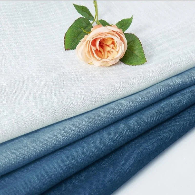 Tissus élégants empilés en plusieurs nuances de bleu et blanc avec une rose délicate posée dessus, parfaits pour des projets de décoration intérieure raffinée.