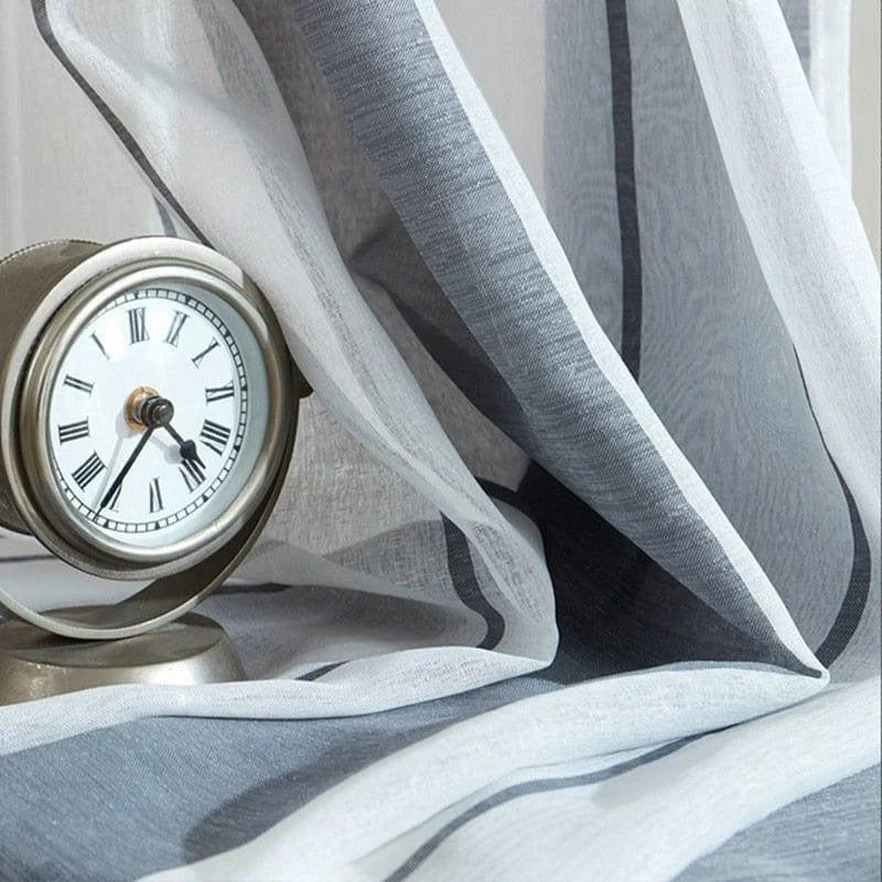 Horloge de style classique avec chiffres romains, posée près d'un rideau élégant de couleur grise et blanche, ajoutant une touche sophistiquée à votre décoration intérieure. Idéal pour un salon ou une chambre moderne.