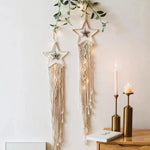 Décoration murale bohème avec étoiles suspendues et motifs élégants, illuminée pour une ambiance chaleureuse. Idéale pour ajouter une touche artistique à votre intérieur. Bougies et feuillage en arrière-plan pour un effet apaisant.