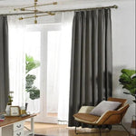 Rideaux élégants de couleur sombre encadrant une porte-fenêtre, apportant une touche moderne et chaleureuse au salon. Décoration intérieure soignée avec plantes vertes en arrière-plan et mobilier contemporain, créant une ambiance harmonieuse idéale pour un espace de vie confortable. Éclairage naturel traversant la pièce, soulignant la sophistication du décor.