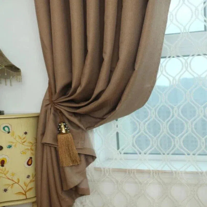 Rideau élégant de couleur marron avec embrasse décorative, installée dans un intérieur contemporain, devant une fenêtre dotée d'un voilage à motifs géométriques, idéal pour ajouter une touche de sophistication à votre salon ou chambre à coucher. Parfait pour personnaliser votre décoration intérieure tout en contrôlant la luminosité.