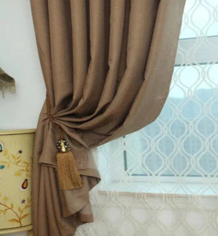 Rideau élégant de couleur marron avec embrasse décorative, installée dans un intérieur contemporain, devant une fenêtre dotée d'un voilage à motifs géométriques, idéal pour ajouter une touche de sophistication à votre salon ou chambre à coucher. Parfait pour personnaliser votre décoration intérieure tout en contrôlant la luminosité.