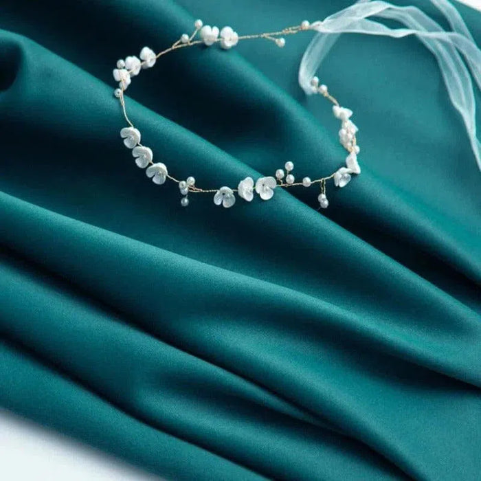 Couronne délicate ornée de fleurs et perles sur fond drapé turquoise, parfaite pour une touche élégante lors de mariages ou occasions spéciales. Accessoire raffiné mettant en valeur l'harmonie des couleurs et le style romantique.