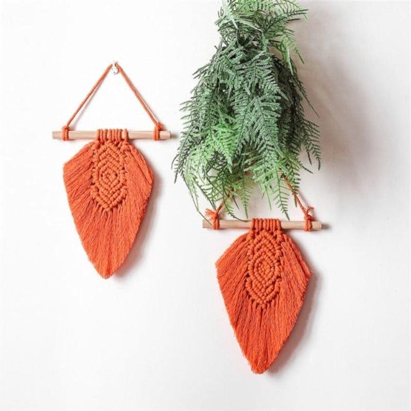 Décoration murale en macramé orange, suspendue avec des bâtons en bois. Idéale pour ajouter une touche bohème à une pièce, elle est accompagnée de verdure pour une ambiance naturelle. Parfaite pour le salon ou la chambre, cette décoration stimule une atmosphère chaleureuse et accueillante.