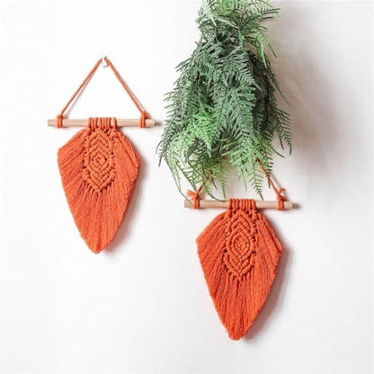 Décoration murale en macramé orange, suspendue avec des bâtons en bois. Idéale pour ajouter une touche bohème à une pièce, elle est accompagnée de verdure pour une ambiance naturelle. Parfaite pour le salon ou la chambre, cette décoration stimule une atmosphère chaleureuse et accueillante.