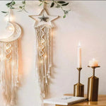 Décoration murale bohème avec tenture en forme de lune et étoile, illustrant un style minimaliste et élégant. Ce design unique apporte une touche chaleureuse et lumineuse à votre intérieur, idéal pour sublimer votre espace avec une ambiance apaisante. Parfait pour le salon, la chambre ou tout espace nécessitant une décoration raffinée. Ces éléments se marient harmonieusement avec des accessoires modernes, comme les chandeliers dorés visibles sur la table en bois, créant