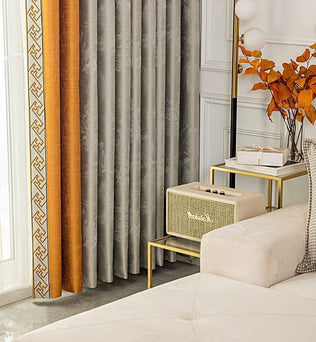 Rideaux modernes gris et orange avec motifs géométriques, ajout élégant à un salon contemporain. Accents dorés sur les tables, vase avec feuilles colorées, offrant une touche automnale. Idéal pour une décoration intérieure sophistiquée et chaleureuse.
