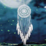 Attrape-rêves artisanal élégant suspendu sous un ciel nocturne étoilé. Ce capteur de rêves blanc est orné de plumes délicates, parfait pour apporter une touche de sérénité et d'élégance à votre décoration intérieure. Idéal pour apaiser vos nuits et ajouter une esthétique bohème à votre chambre.