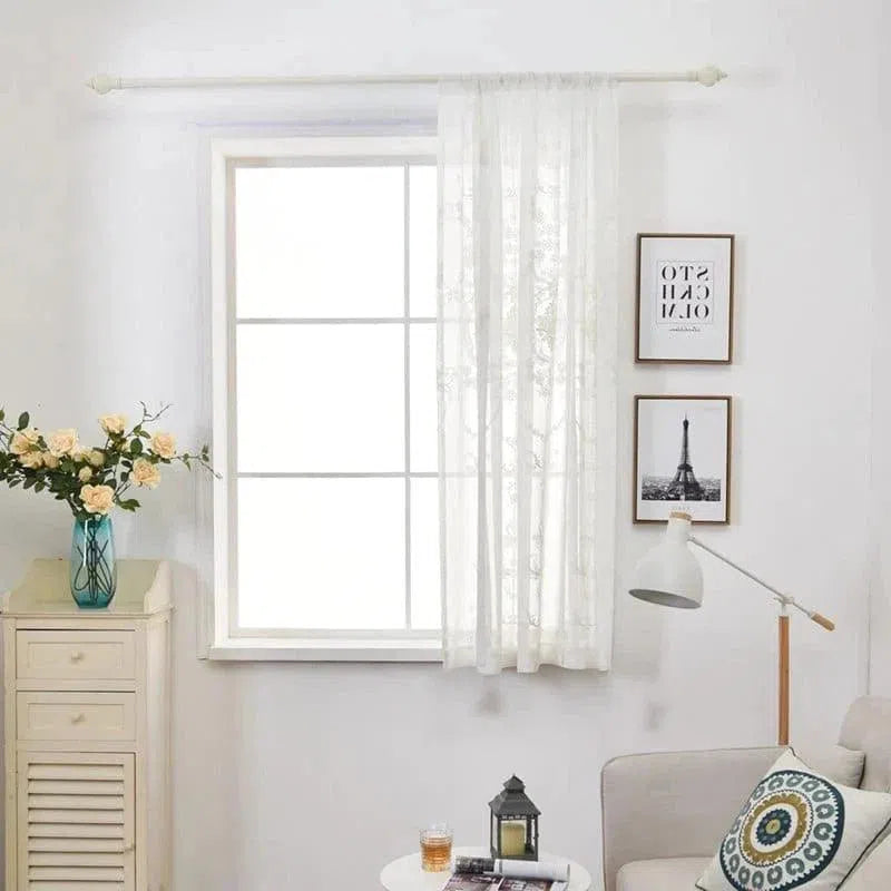 Rideaux blancs transparents suspendus à une fenêtre lumineuse dans un salon moderne. Décor épuré avec une lampe de lecture, un canapé confortable, et un coussin orné de motifs géométriques. Des cadres élégants et un vase avec des fleurs jaunes complètent l'ambiance accueillante et sophistiquée de cet espace. Idéal pour améliorer la luminosité et l'élégance de votre intérieur.