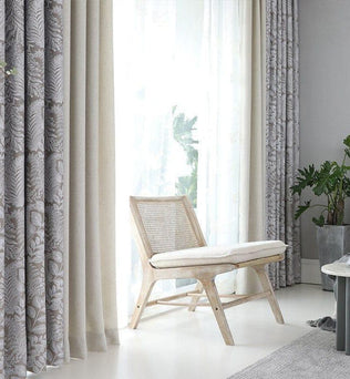 Coin détente élégant avec chaise bois clair, rideaux américains à motifs et rideaux unis, sur fond de lumière naturelle abondante.