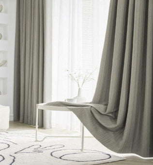 Rideaux élégants gris dans un salon moderne, accentuant une décoration intérieure minimaliste avec un tapis graphique et une table blanche. Ambiance lumineuse et sereine pour un espace de vie contemporain.