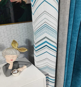 Rideaux modernes avec motifs géométriques bleu et gris, parfaits pour un salon contemporain. Design élégant avec statue décorative et tasse sur table blanche. Idéal pour rehausser la décoration intérieure et ajouter une touche de couleur et de style.