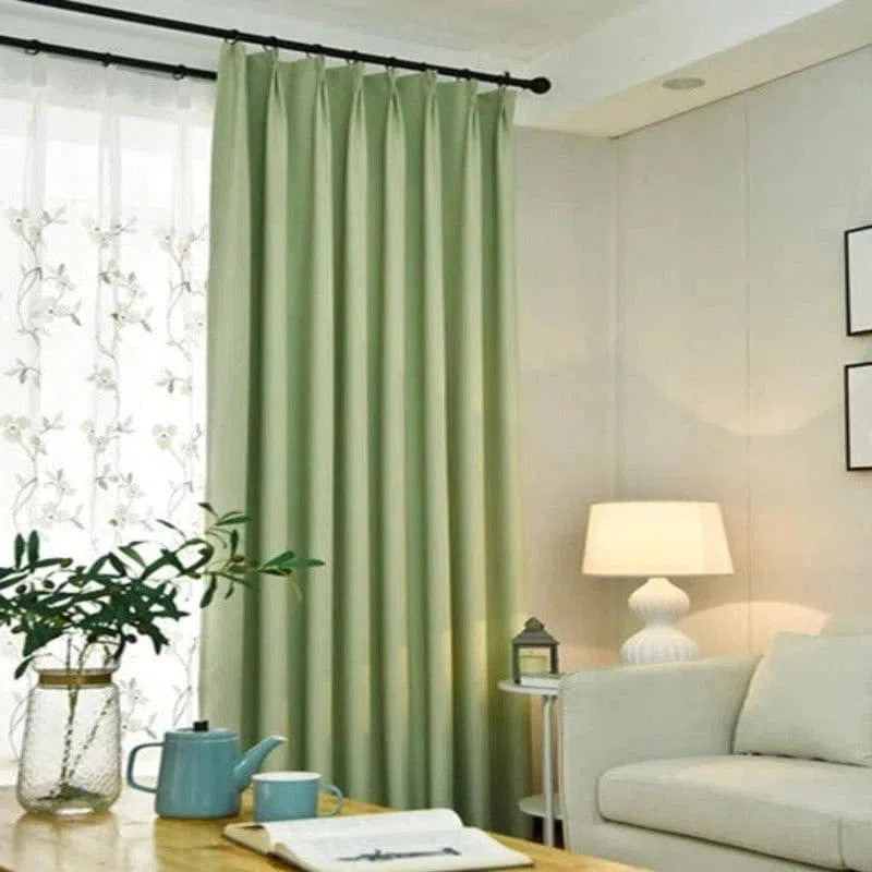 Rideau vert élégant dans un salon moderne. Ce rideau offre une touche de fraîcheur à la décoration intérieure, créant une ambiance relaxante et harmonieuse. Installé sur une tringle noire classique, le rideau se marie parfaitement avec le mobilier du salon, comprenant un canapé beige, une lampe de table au design sophistiqué et des accessoires décoratifs assortis. Idéal pour compléter et personnaliser l'espace de vie.