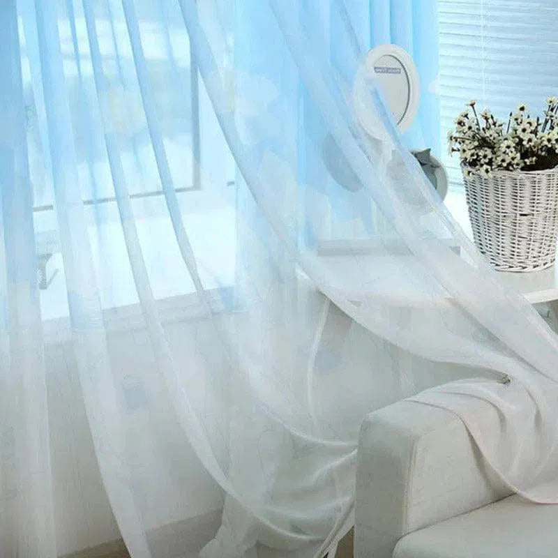 Voilage blanc transparent flottant élégamment devant une fenêtre, créant une ambiance lumineuse et aérienne dans un salon moderne. Idéal pour tamiser la lumière naturelle tout en préservant l'intimité. Accessoire parfait pour une décoration intérieure chic et minimaliste.