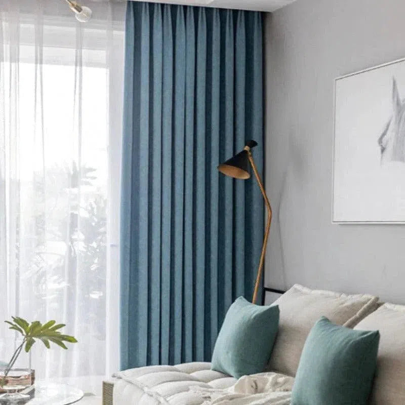 Rideaux modernes bleu canard suspendus dans un salon élégant avec un canapé confortable et une lampe dorée. Idéal pour une décoration intérieure contemporaine et apaisante. Classe et sobriété pour un espace de vie harmonieux.