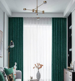 Salon élégant avec rideaux verts et lampadaire moderne. Canapé confortable orné de coussins colorés, table basse avec vase décoratif. Luminaire suspendu stylé, combinant design contemporain et douceur naturelle. Idéal pour une décoration intérieure harmonieuse. Parfait pour créer une ambiance chaleureuse et accueillante dans un espace de vie raffiné.