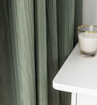 Rideaux verts élégants tombant harmonieusement à côté d'une table blanche moderne avec un verre vide, apportant une touche de sophistication à la décoration intérieure.