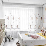 Chambre d'enfant lumineuse avec décoration douce. Rideaux transparents avec motifs de petites danseuses, laissant entrer la lumière naturelle. Lit blanc avec linge aux motifs étoilés, jouets en peluche et éléments ludiques pour un espace accueillant et joyeux. Parfait pour créer une ambiance apaisante et rêveuse dans une chambre de petite fille.