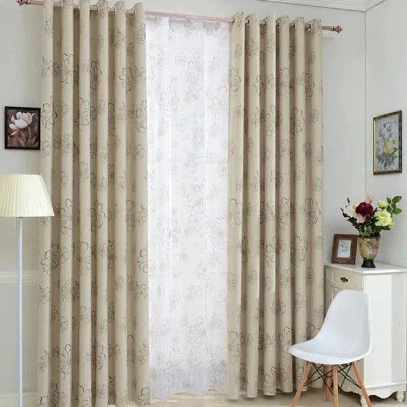 Rideau beige à motifs floraux, installé dans un salon moderne avec décoration élégante, comprenant une lampe, des tableaux et des fleurs sur une commode blanche.