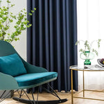 Fauteuil à bascule design en bleu avec coussin assorti, situé dans un salon moderne. Les rideaux sombres ajoutent une touche d'élégance, tandis que la table dorée avec vase vert apporte une touche de fraîcheur. Un espace idéal pour se détendre et lire dans un cadre harmonieux et stylé.
