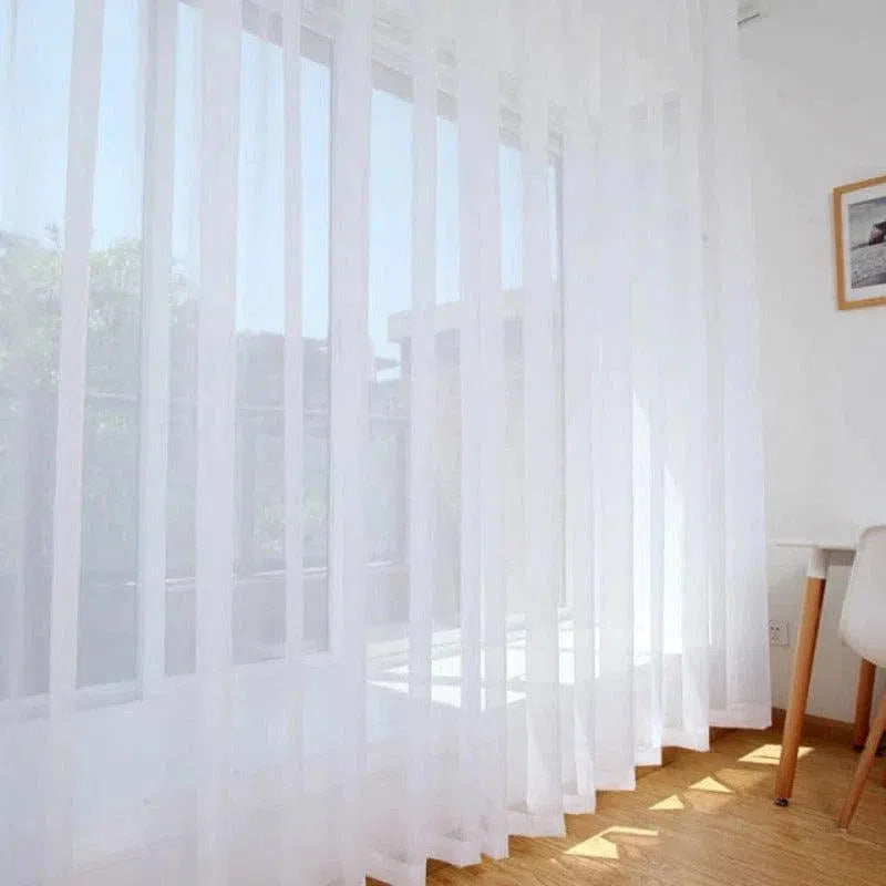 Rideau blanc transparent suspendu dans une pièce lumineuse, laissant entrer la lumière naturelle tout en préservant l'intimité. Design élégant et minimaliste, idéal pour salon moderne ou chambre à coucher. Ajustement parfait pour des fenêtres larges, ajoutant une touche de sophistication à la décoration intérieure.