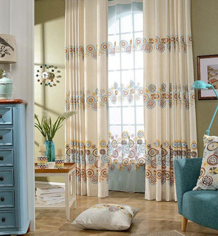 Rideaux élégants avec motifs floraux colorés pour salon moderne, ajoutant une touche de charme et de luminosité à votre intérieur. Idéal pour décorer un espace de vie accueillant et chaleureux. Coussin assorti au design floral vibrant, complétant harmonieusement la décoration du salon. Meuble et lampe bleus accentuant le style contemporain de la pièce. Vitrine et accessoire décoratif ajoutant une ambiance cosy et raffinée.