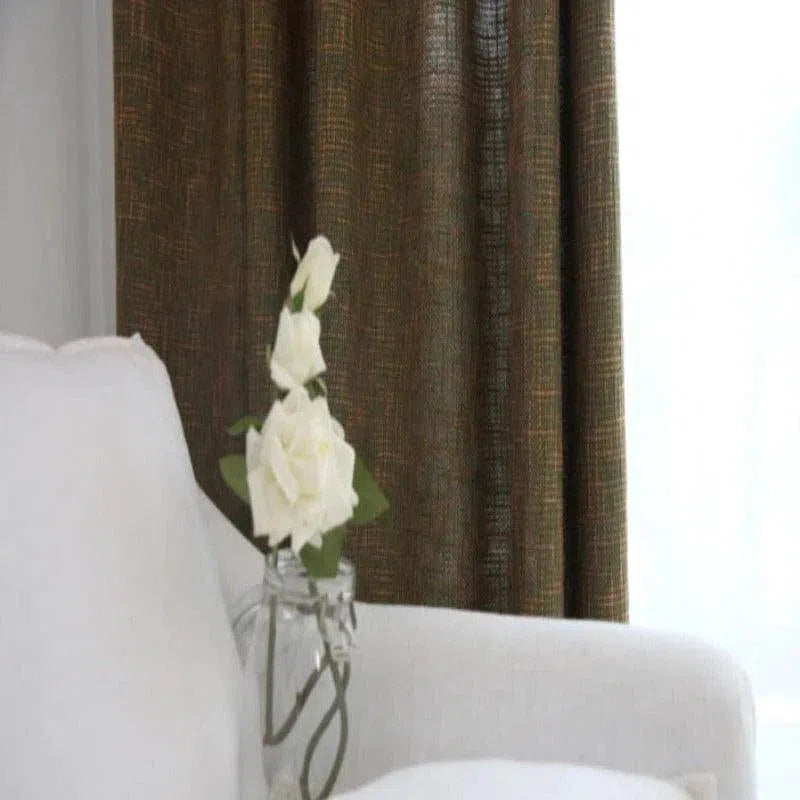 Une élégante chambre à coucher décorée avec des rideaux marron texturés, apportant une touche chaleureuse et moderne à l'espace. Un vase transparent avec des fleurs blanches fraîches est posé sur un fauteuil blanc, ajoutant une note délicate et naturelle à l'ensemble du décor.