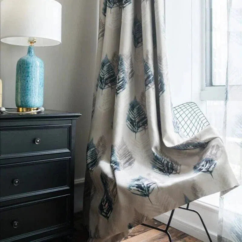 Rideau design motif plume dans un salon moderne, suspendu à côté d'une fenêtre lumineuse, accompagné d'une table noire avec lampe décorative bleue. Idéal pour ajouter une touche élégante et naturelle à votre intérieur.
