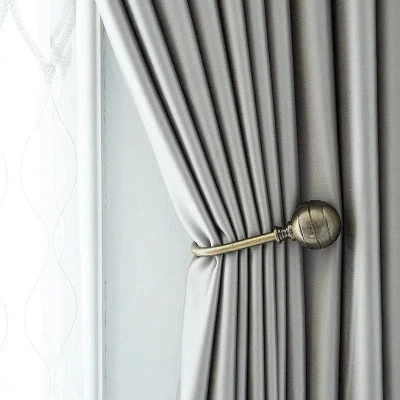 Rideau élégant gris clair attaché avec une embrasse décorative en métal doré, idéal pour ajouter une touche de raffinement à votre intérieur. Convient parfaitement aux styles modernes et classiques, optimisant la luminosité de la pièce tout en offrant une intimité contrôlée.