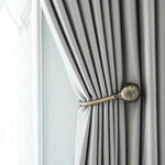 Rideau élégant gris clair attaché avec une embrasse décorative en métal doré, idéal pour ajouter une touche de raffinement à votre intérieur. Convient parfaitement aux styles modernes et classiques, optimisant la luminosité de la pièce tout en offrant une intimité contrôlée.