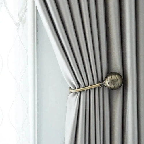 Rideau élégant gris clair attaché avec une embrasse décorative en métal doré, idéal pour ajouter une touche de raffinement à votre intérieur. Convient parfaitement aux styles modernes et classiques, optimisant la luminosité de la pièce tout en offrant une intimité contrôlée.