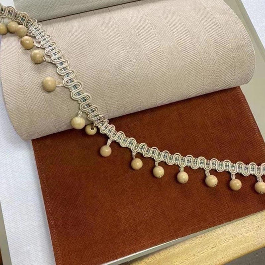 Deux échantillons de tissu, un beige et un marron, sont présentés avec une garniture à pompons décoratifs. Parfait pour une décoration intérieure élégante et chaleureuse.