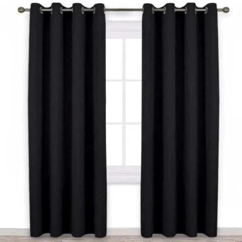 Rideau occultant noir élégant suspendu devant une fenêtre. Idéal pour bloquer la lumière et offrir une isolation thermique dans votre salon ou chambre. Design moderne avec œillets métalliques pour une installation facile. Parfait pour ajouter une touche sophistiquée à votre intérieur.