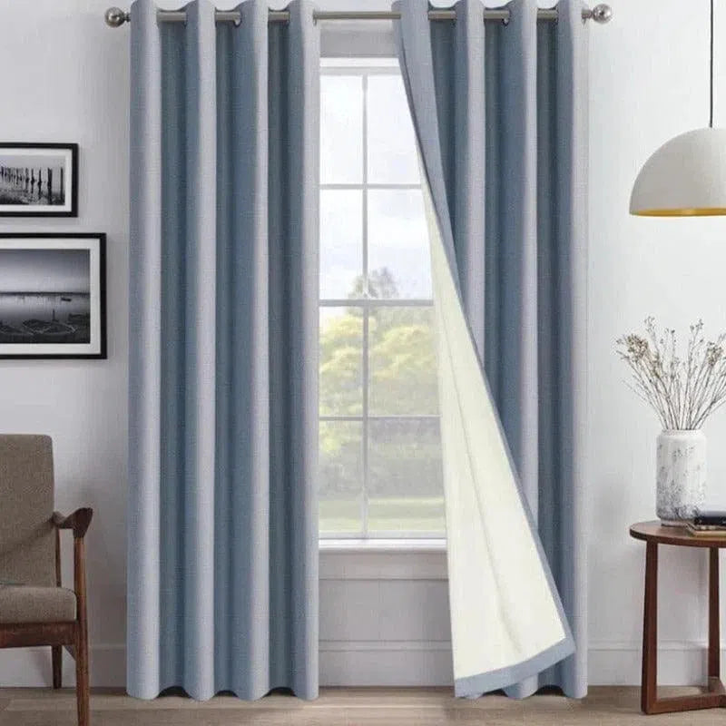 Rideaux occultants gris bleuté pour salon moderne, élégamment accrochés devant une grande fenêtre. Design contemporain avec des œillets métalliques, ces rideaux ajoutent une touche de sophistication et de fonctionnalité, parfaits pour un intérieur lumineux et stylé.